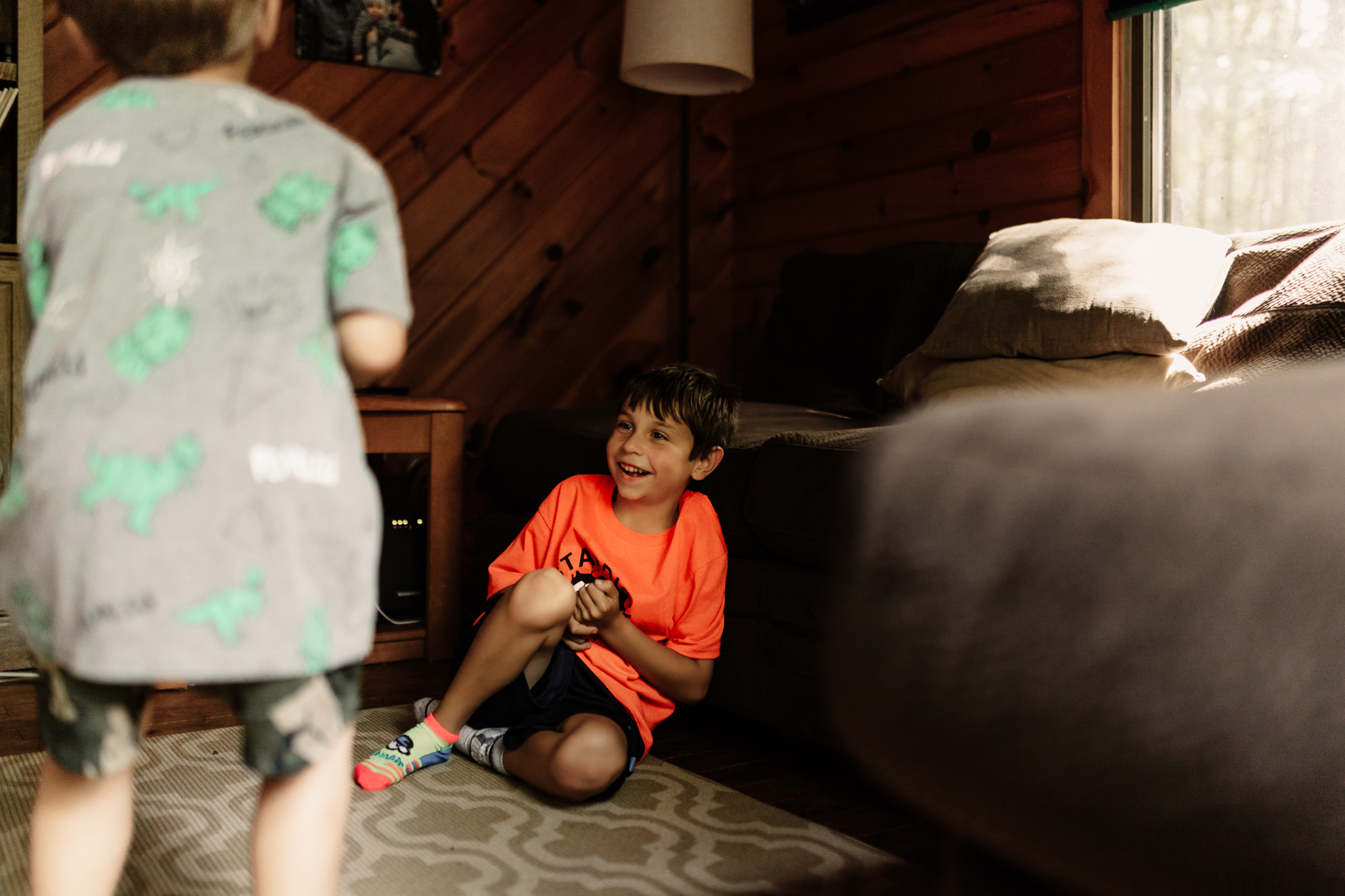 A young boy laughing at his brother in their home during a family photography session in Sebago Lake, Maine