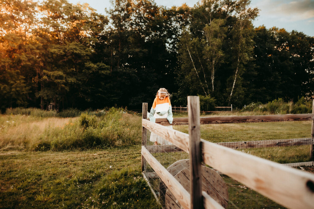 A young girl standing on the fence at her homestead in Bridgton, Maine