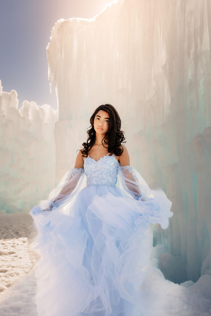 A girl stands in front of an ice wall at the New Hampshire Ice Castles in glowing sunlight