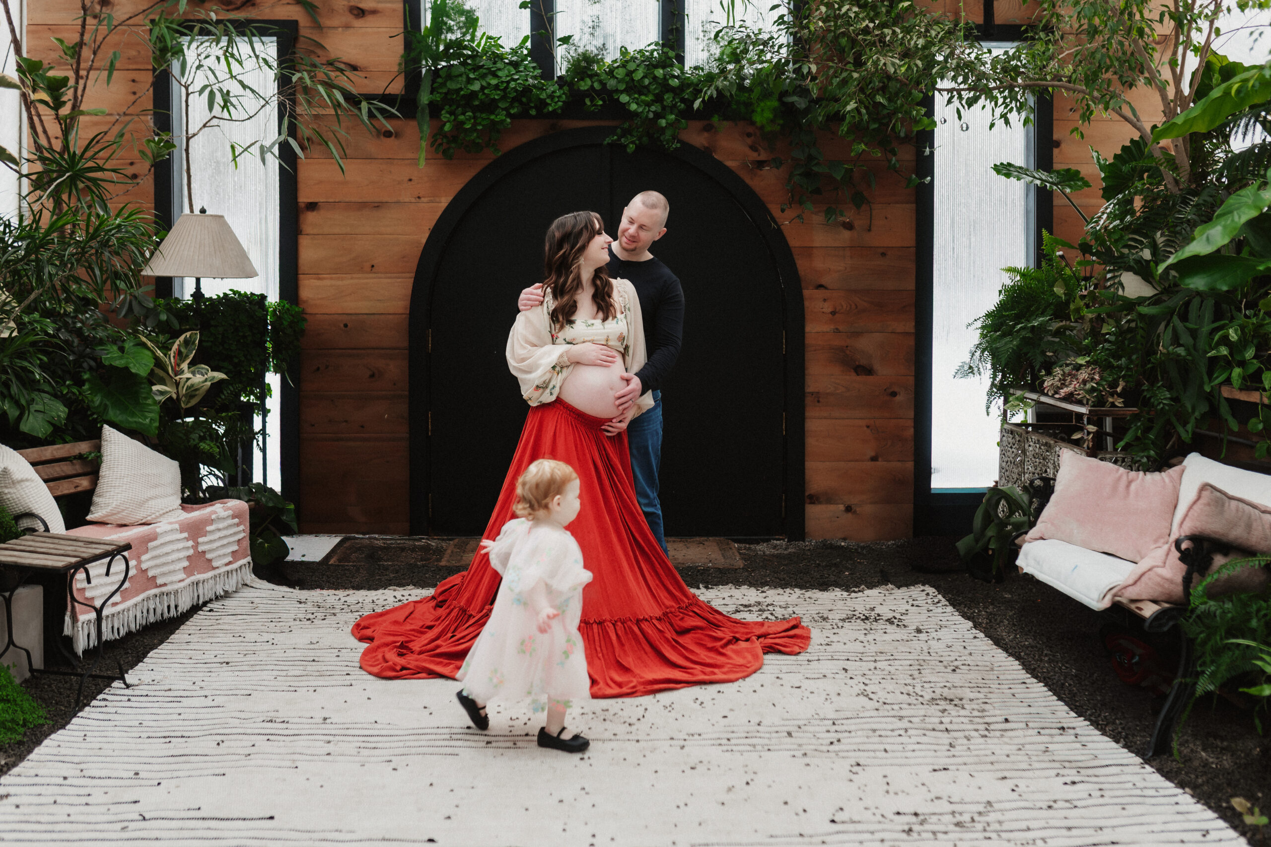 A child runs around her parents during a greenhouse maternity session 